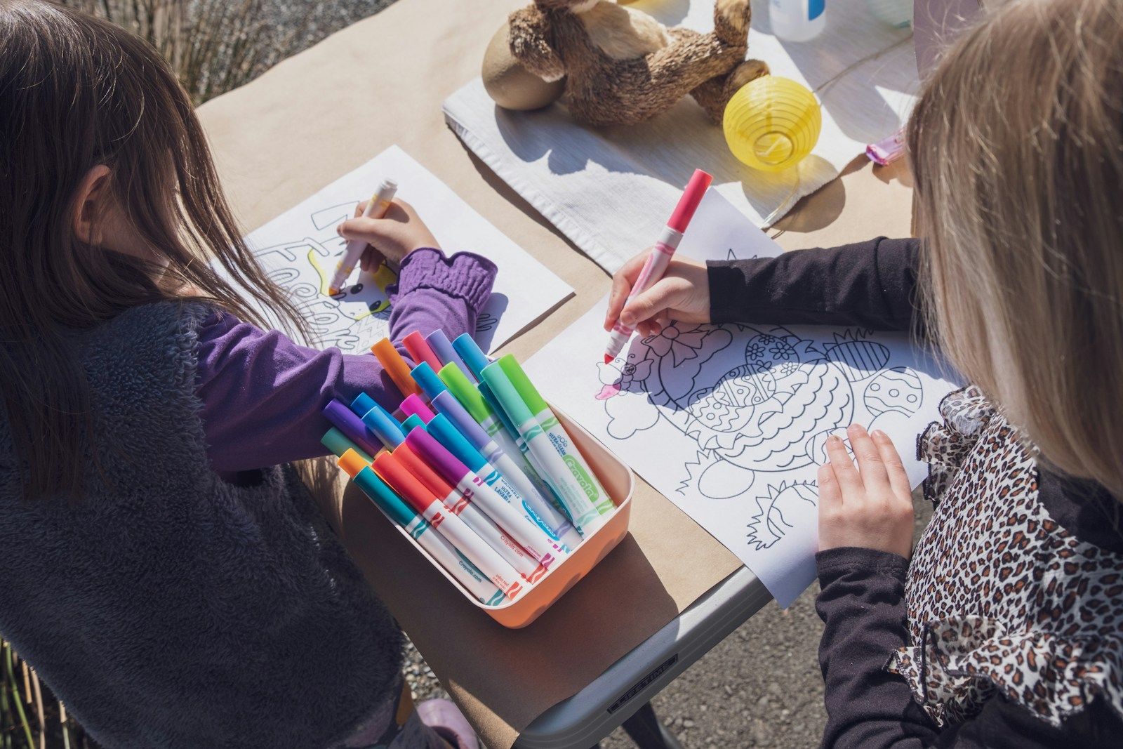 two young girls sitting at a table with markers and crayons